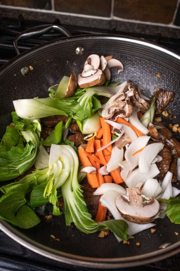 Chopped veggies is being cooked in a wok over beef. 