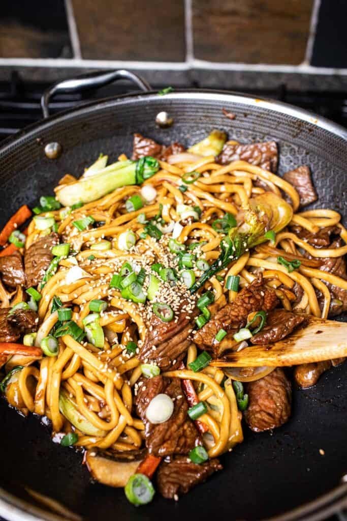 Sesame seeds and green onions over beef udon noodles stir-fry in a wok. 
