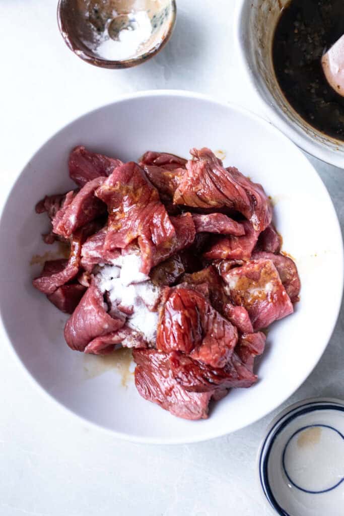 Sliced beef in a bowl with sauce and baking soda. 