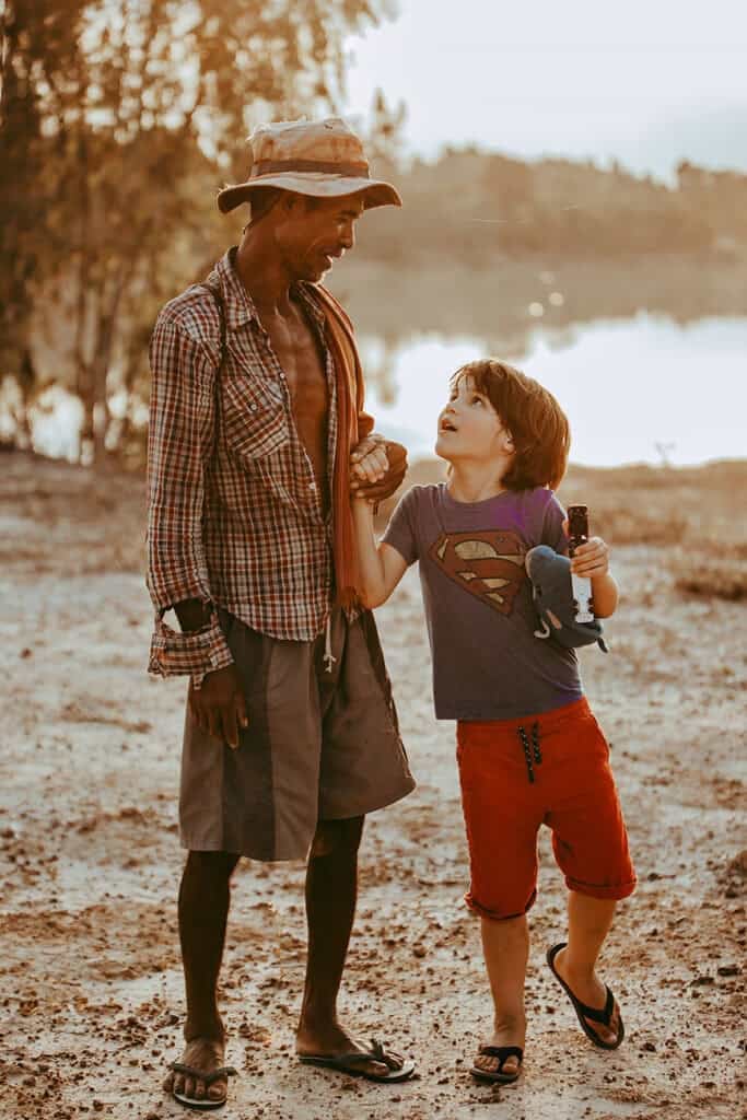 A Thai man holding a young Caucasian boy's hand and smiling. 