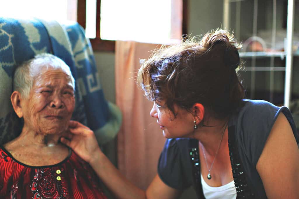 A woman holding an elderly woman's face in her hand while she's crying. 