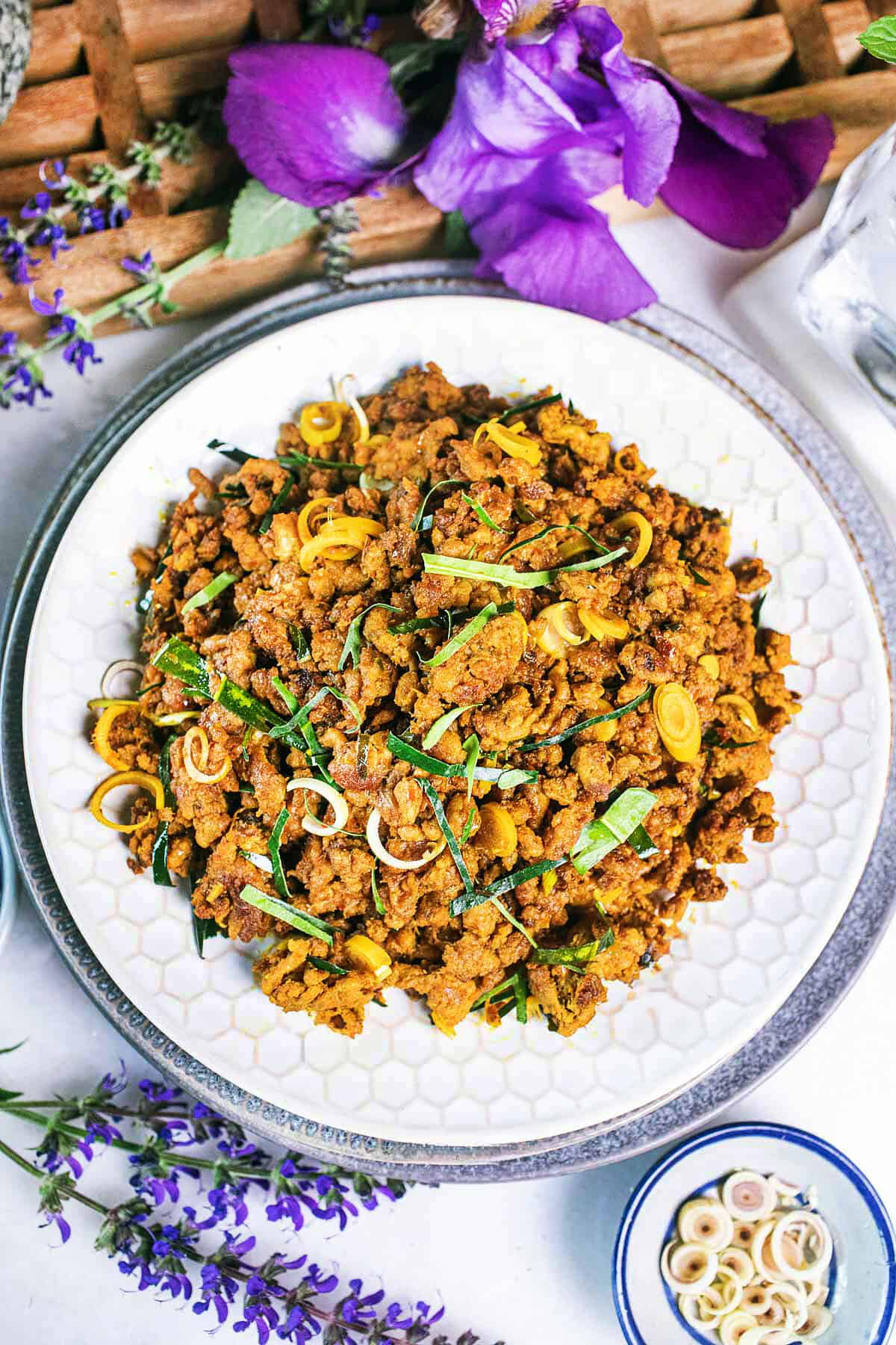 Yellow colored Ground meat curry, with herbs sprinkled on top, on plates stacked on top of each other with flowers around the side.