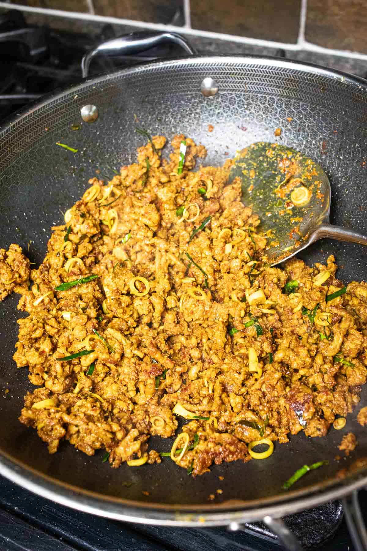 Southern Thai curry with ground pork frying in a wok over the stovetop.