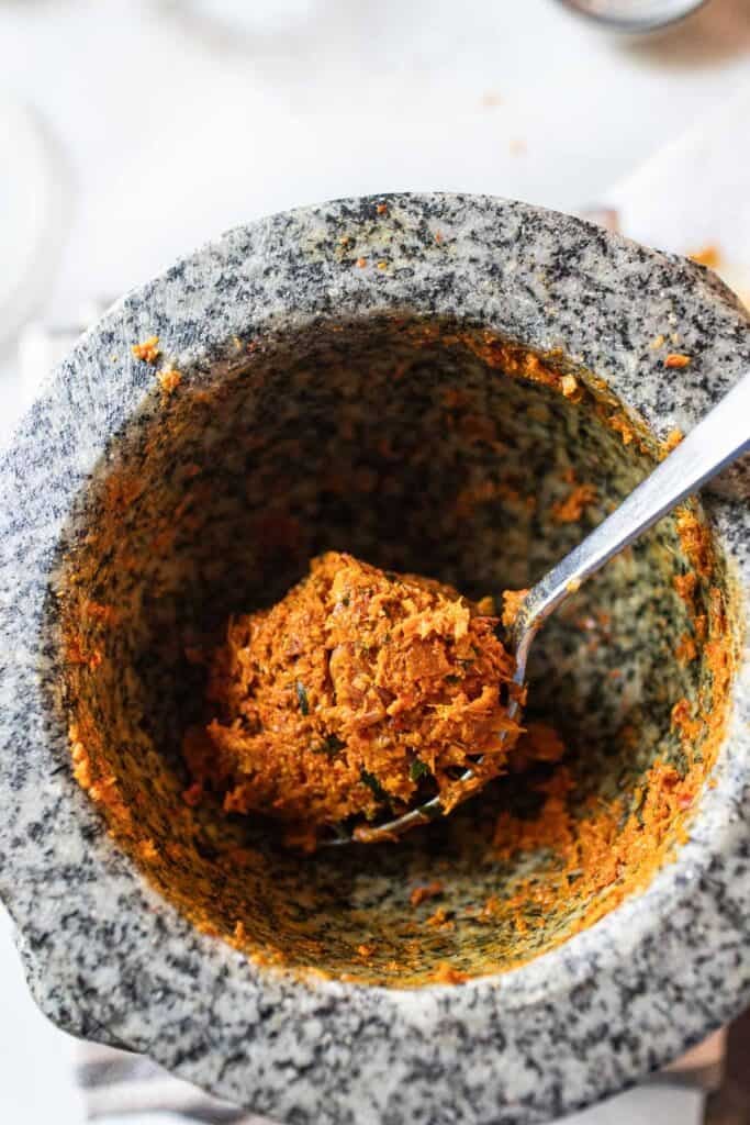 A spoon lifting khua kling paste in a stone mortar and pestle. 