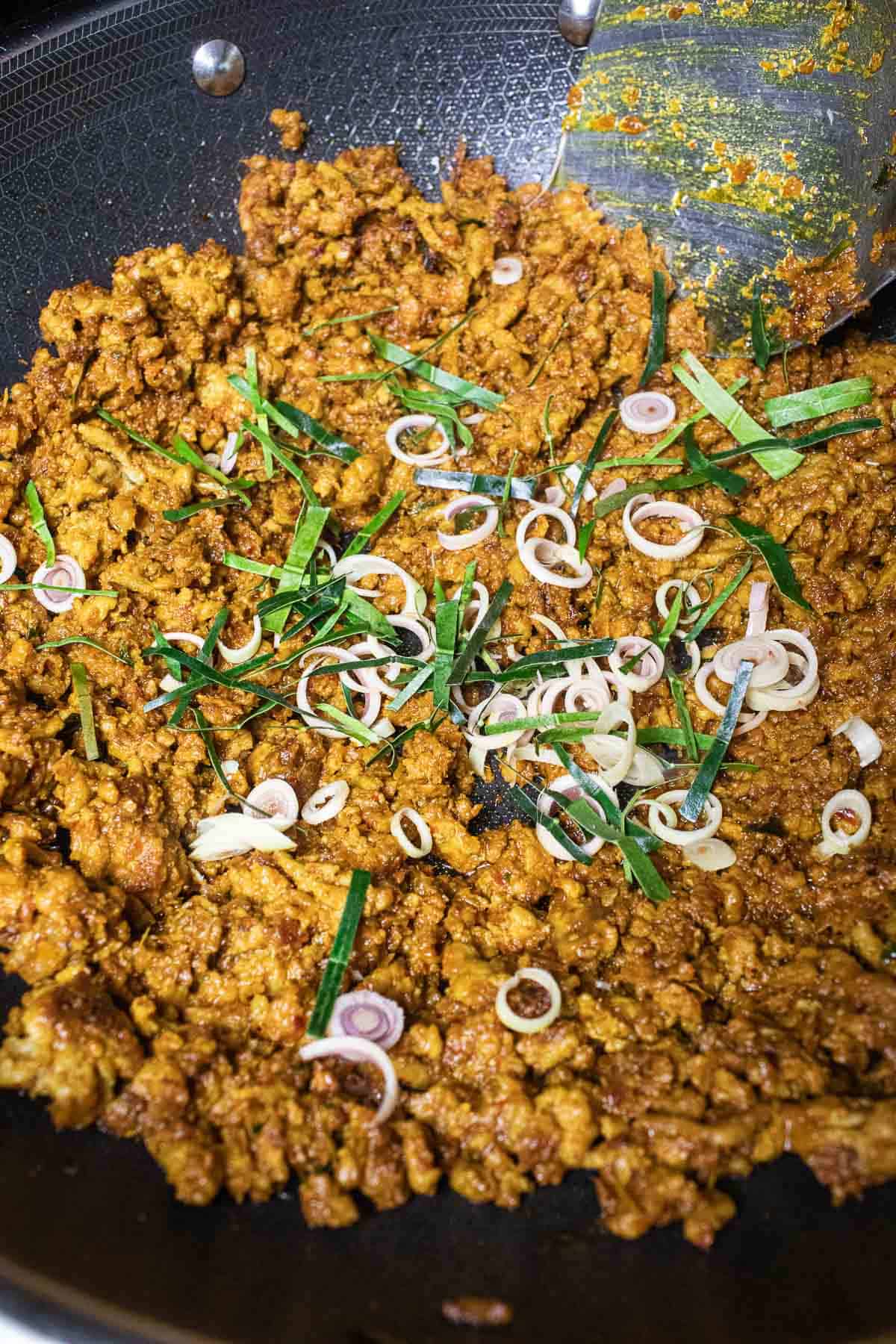 Pork mince curry frying in a wok, over the stovetop,  with herbs on top.