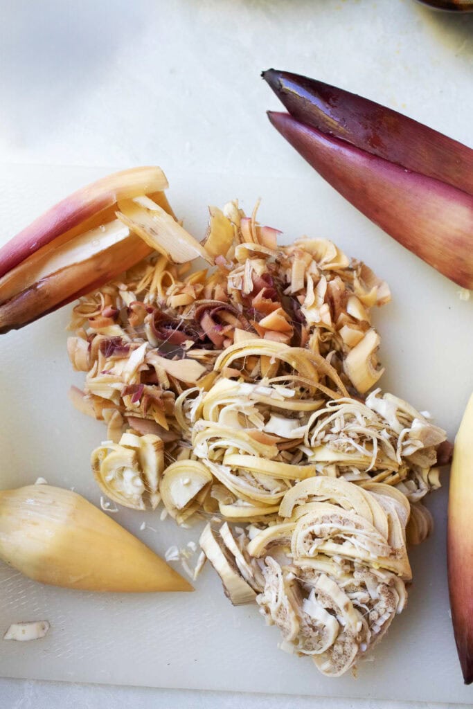 Freshly sliced banana heart and chopped banana blossom petals on a white cutting board, prepped and ready for a Thai salad.