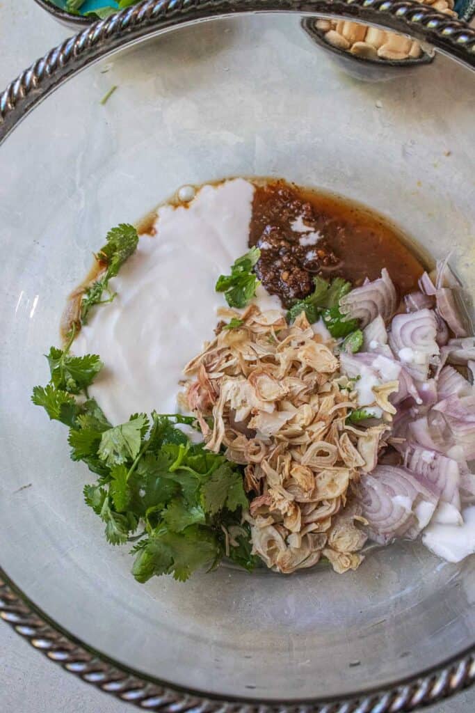 Thai banana blossom salad dressing ingredients in a bowl, including coconut milk, Nam Prik Pao, herbs, shallots, and fried shallots.