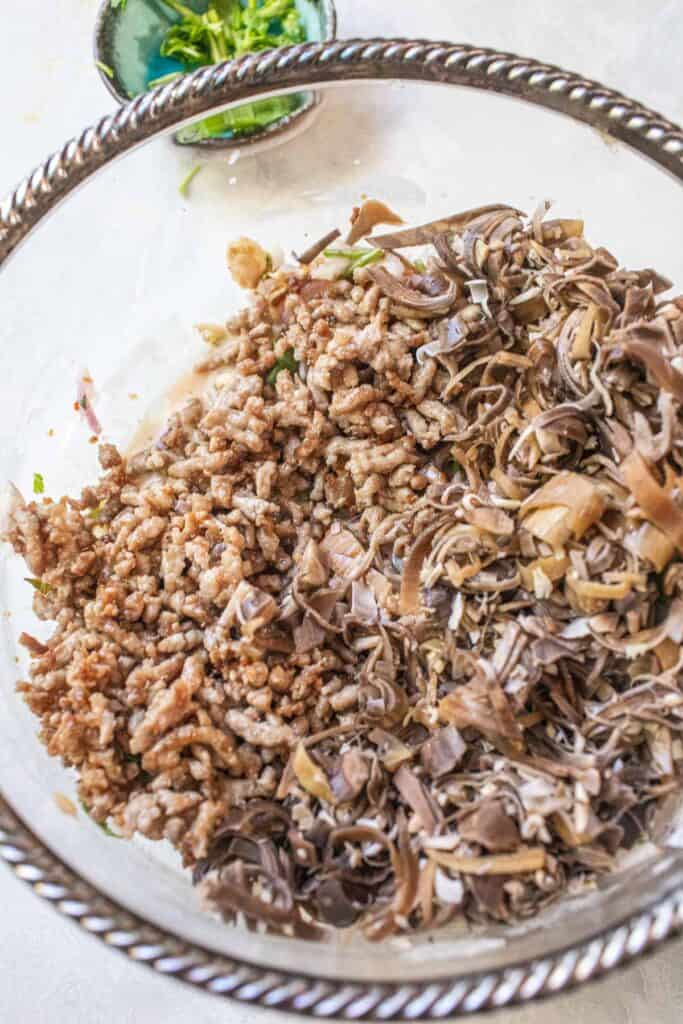 Cooked ground pork and blanched banana blossoms side-by-side in a mixing bowl, ready to be tossed into a Thai banana flower salad.