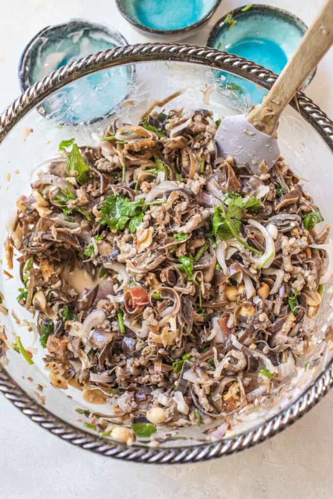 Fully mixed Thai banana blossom salad with herbs, shallots, peanuts, and pork in a large bowl—colorful and packed with texture.