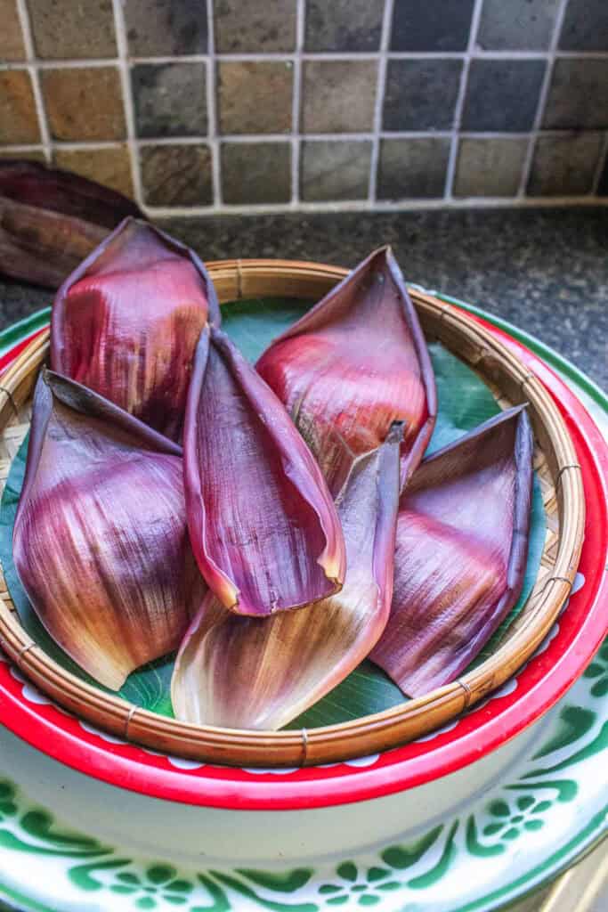 Banana blossom petals neatly arranged in a bamboo tray, prepped for serving Thai banana heart salad in individual petal cups.