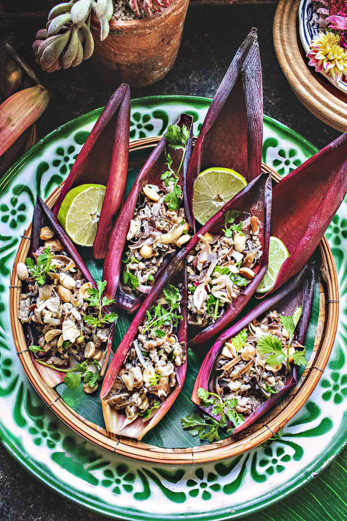 Overhead shot of a traditional Thai banana blossom salad displayed in banana flower petals with bright green herbs and citrus on a green tray.