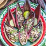 Thai banana blossom salad served in banana heart petals, garnished with peanuts, fresh herbs, and lime wedges on a traditional red tray.
