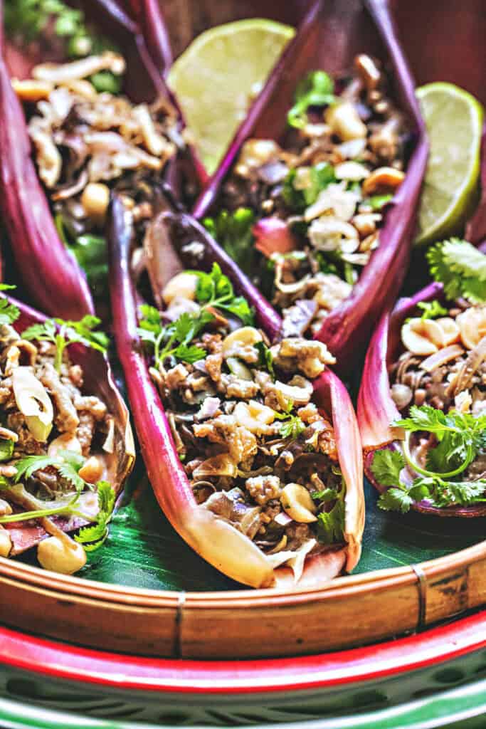 Flat lay of ingredients for Thai banana blossom salad including coconut milk, herbs, ground pork, peanuts, seasonings, and sliced banana hearts.