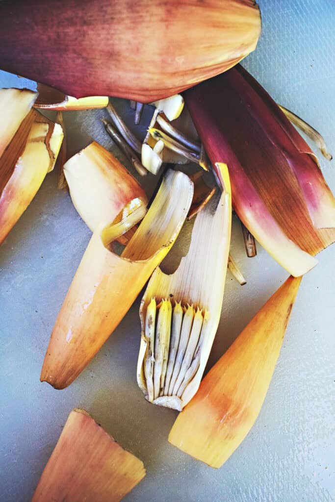 Outer petals and inner layers of banana blossoms peeled and scattered on a cutting board, showing the process of prepping banana heart for Thai salad.