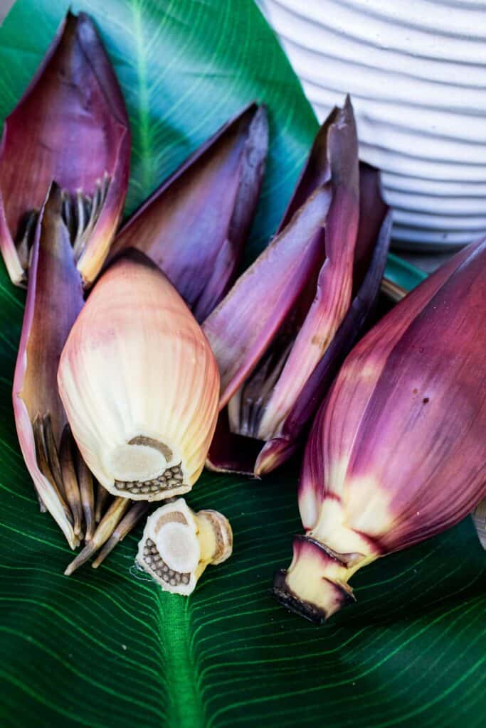 Whole and sliced banana blossoms resting on a large green leaf, showcasing the raw ingredients used in Thai banana blossom salad.