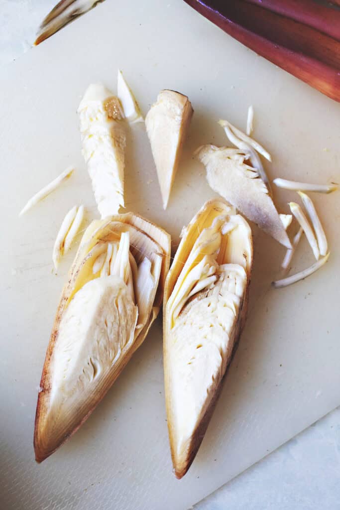 Peeled and halved banana hearts on a cutting board showing fibrous texture and tender shreds inside, part of Thai salad preparation.