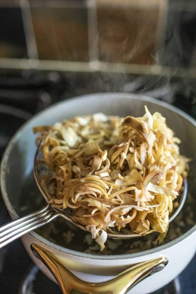 Blanching sliced banana blossoms being lifted from boiling water with a slotted spoon—an essential step to soften and remove bitterness.