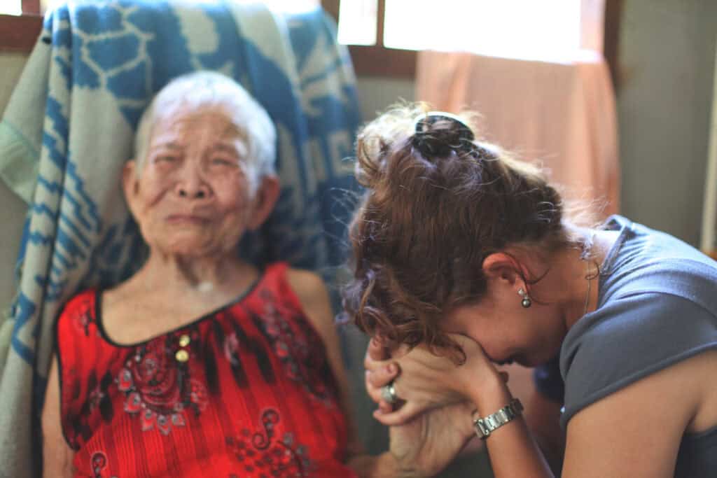A woman holding an elderly woman's hand in her face while crying. 