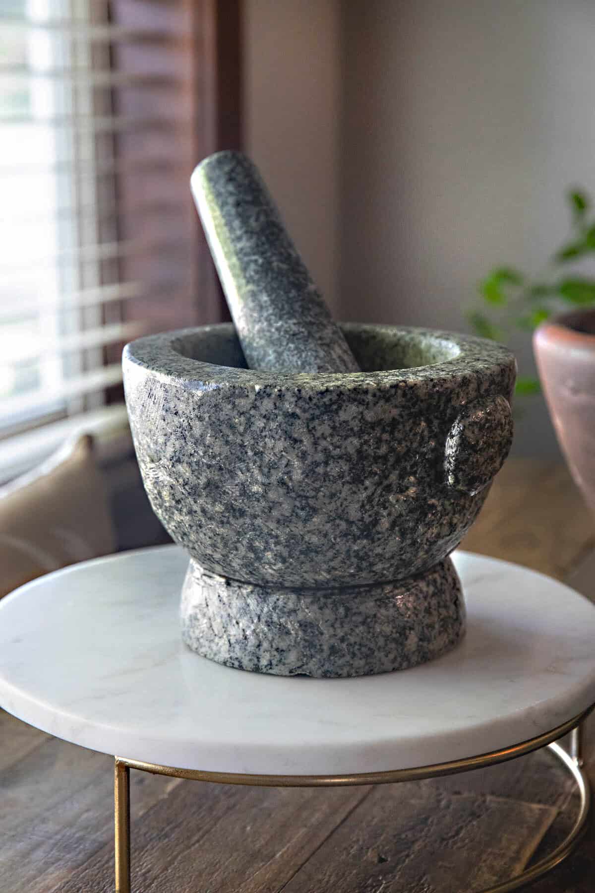 A gray granite mortar and pestle on a cutting board next to a windowsill.