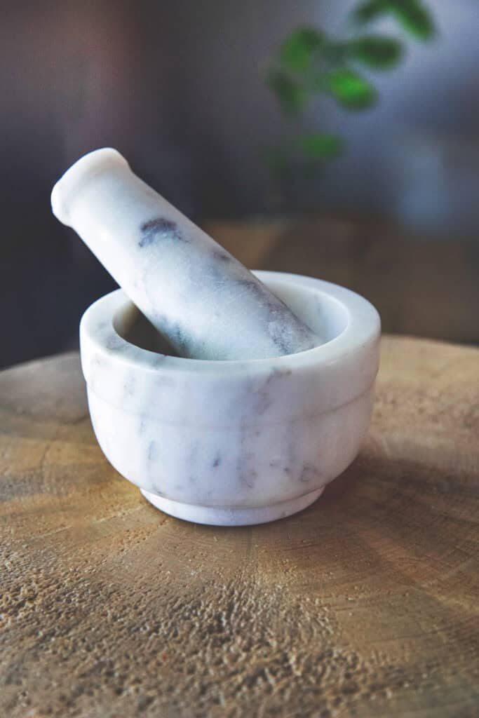 White marble mortar and pestle on a cutting board.