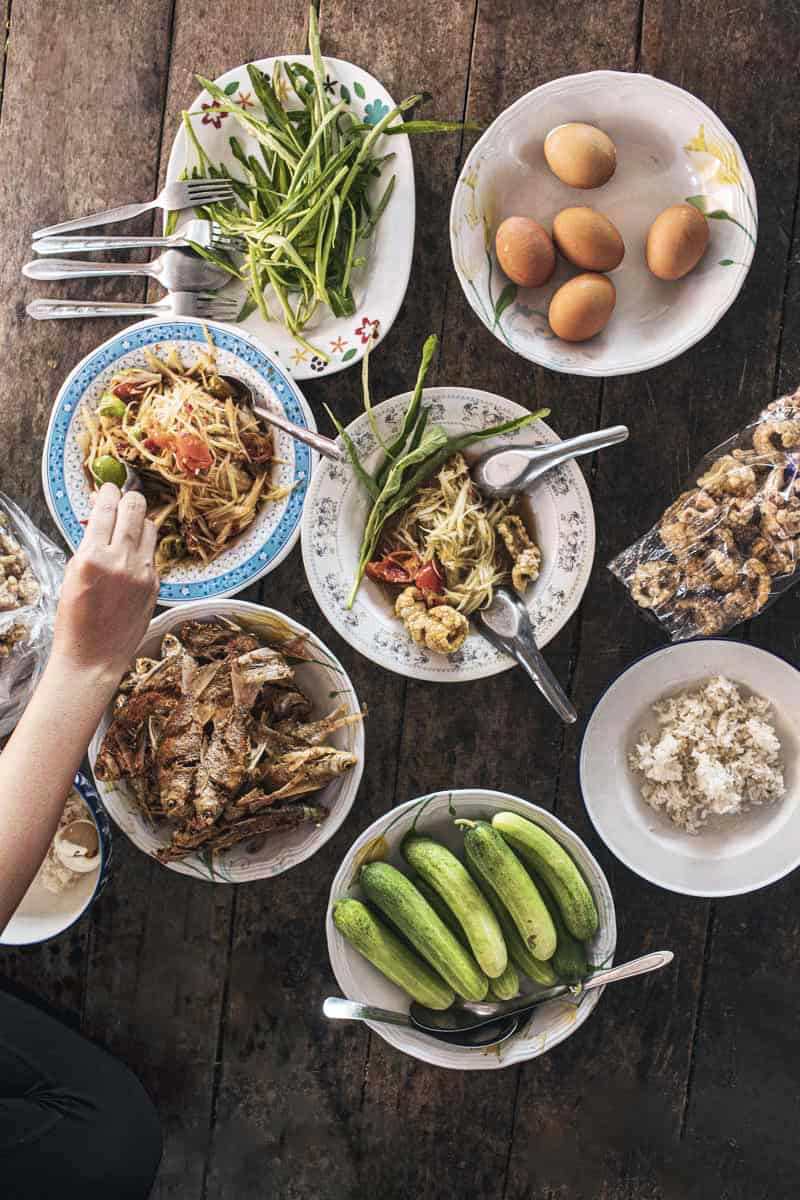Several Thai dishes on a table with a hand grabbing food.