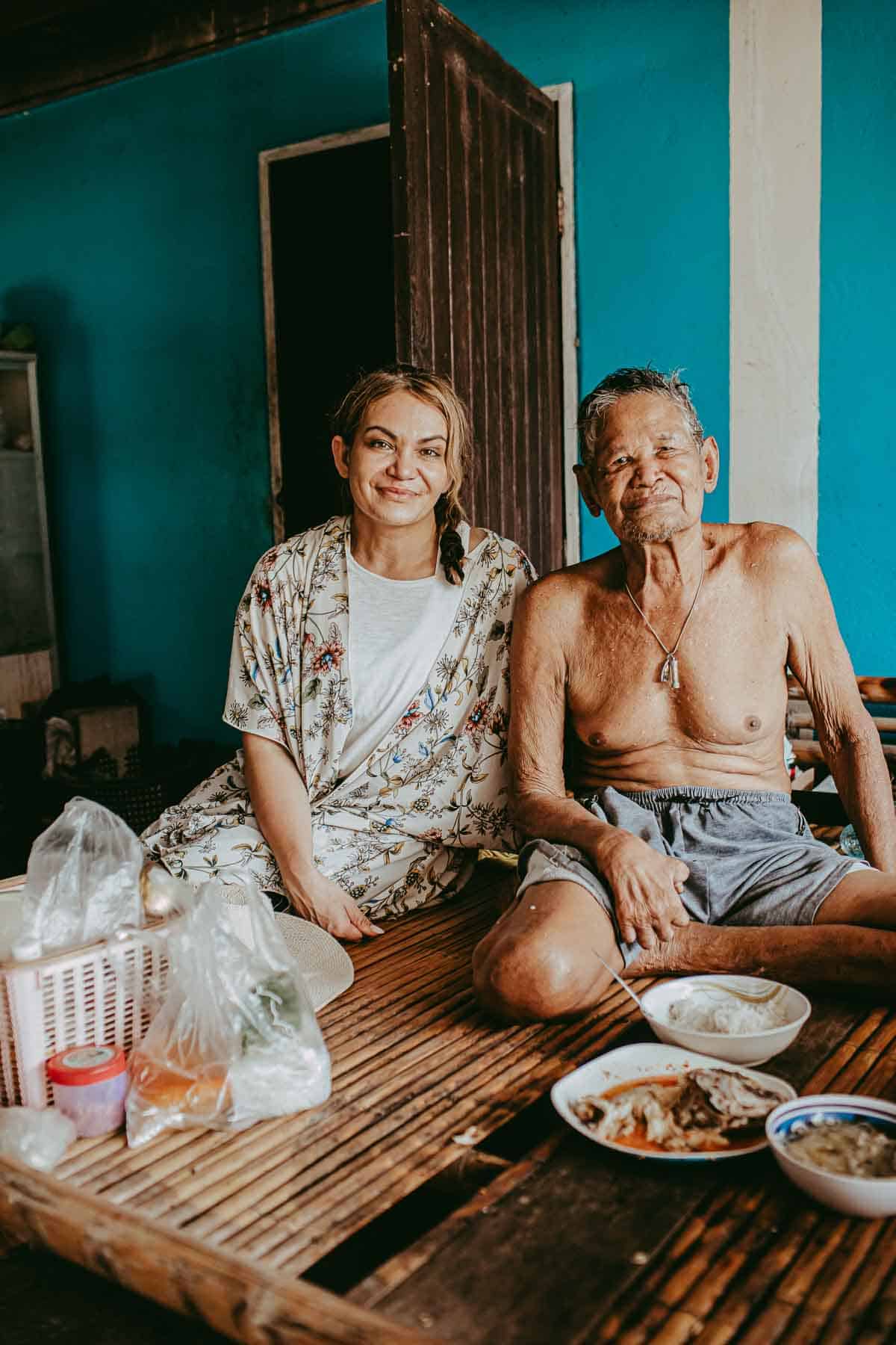 A woman sitting next to an elderly man, hand with him, having food in front of him.