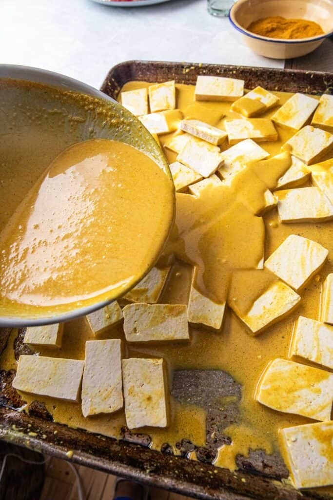Sauce pouring over tofu pieces on a baking tray.