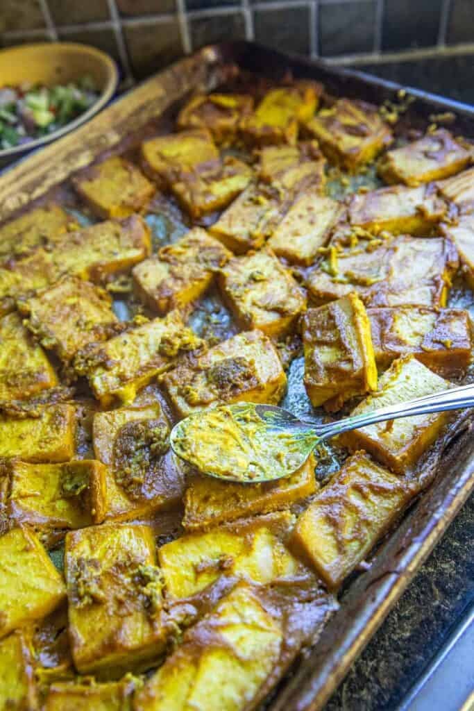 Baked tofu satay on a tray with a spoon on top.