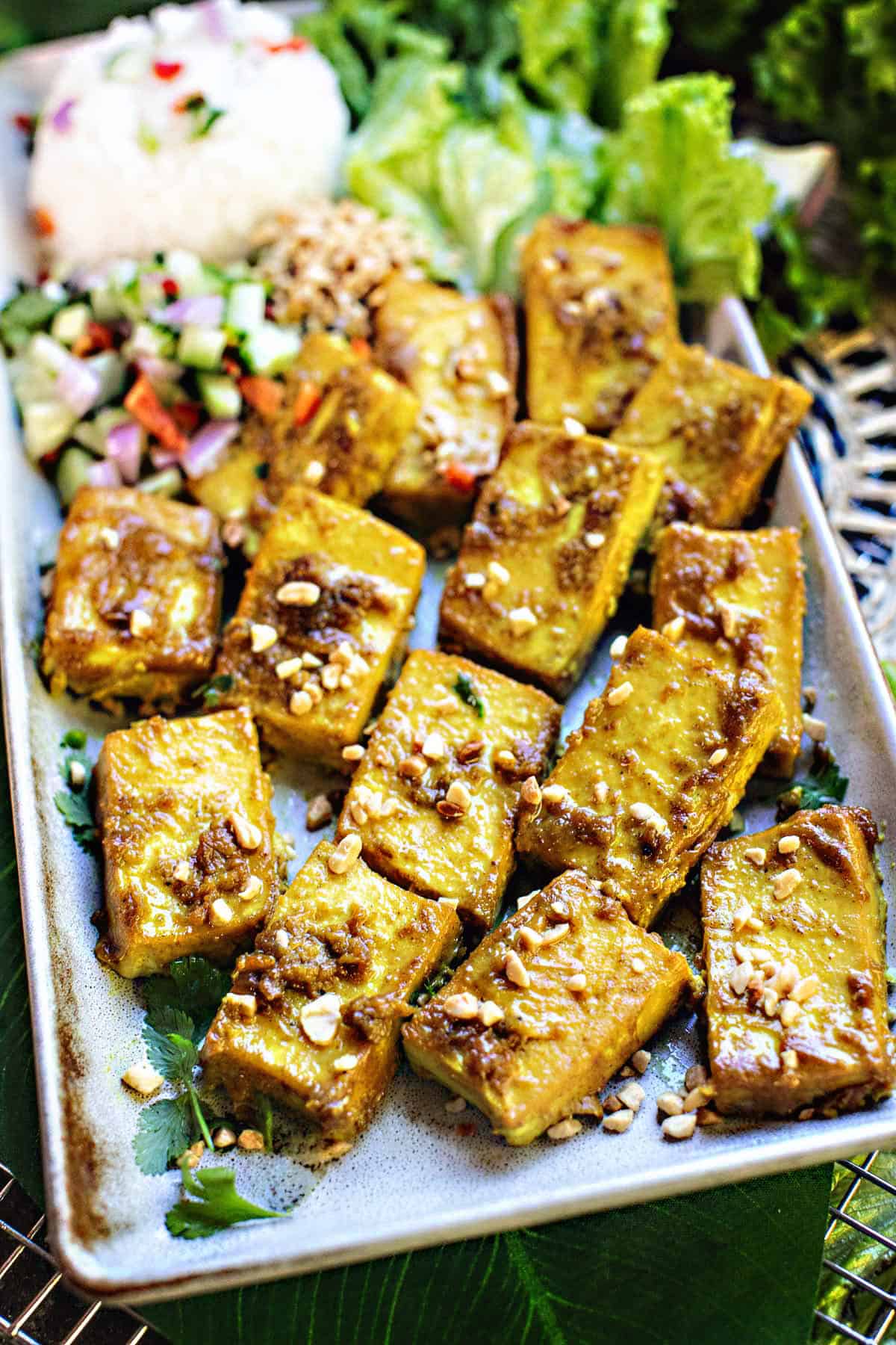 Baked tofu satay on a tray with garnishes.