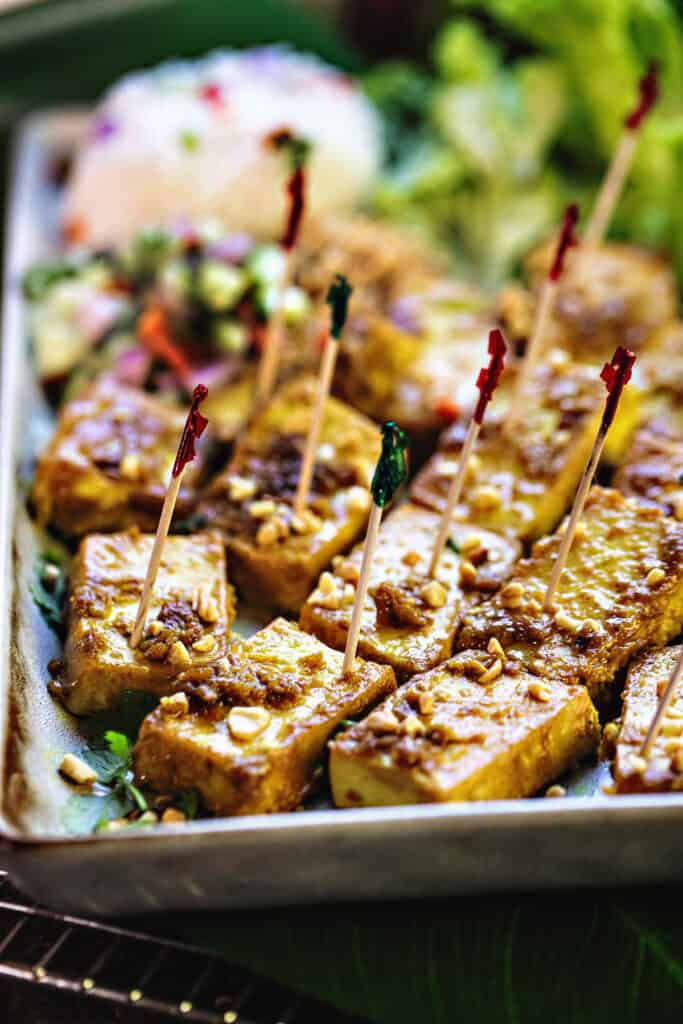 Cooked satay tofu on a platter with tootpicks.