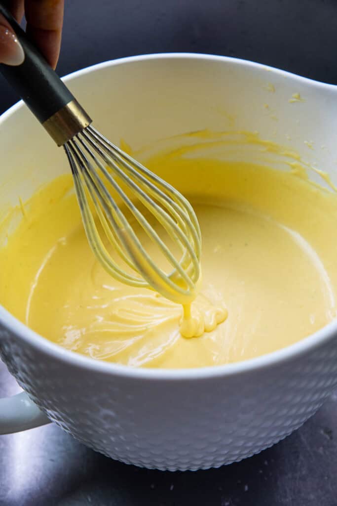 Thai mango ice cream base in a white mixing bowl with a whisk inside. 