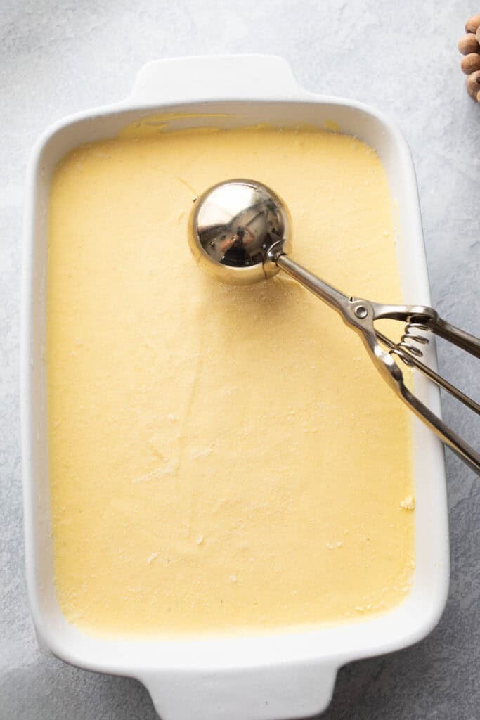 Homemade Asian mango ice cream in a shallow pan with an ice cream scoop on top.