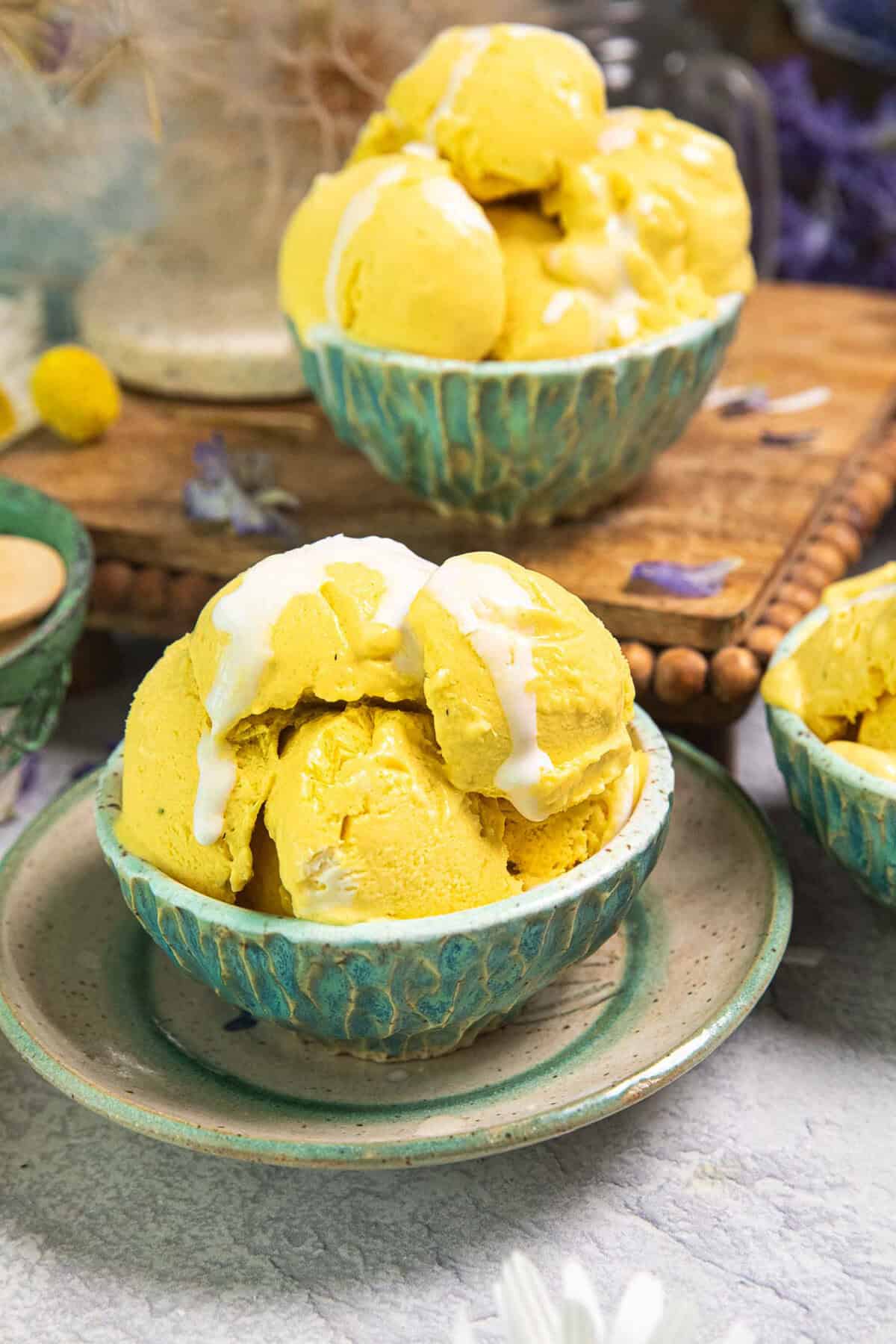 2 bowls of mango ice cream scoops in small green bowls on a table.