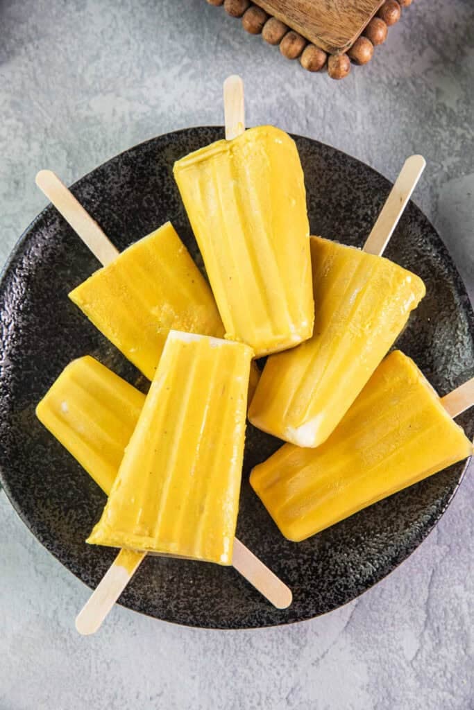 Mango popsicles in sticks on top of each oher on a plate. 