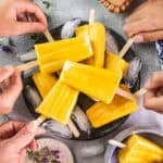 little hands grabbing mango popsicles from a plate.