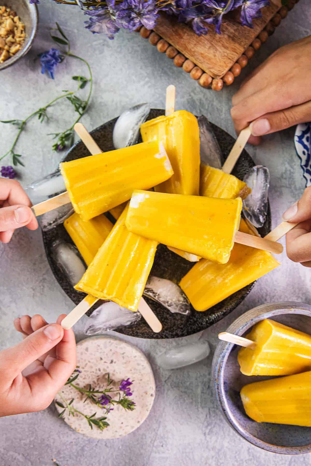 Hands grabbing mango ice pops from a plate.