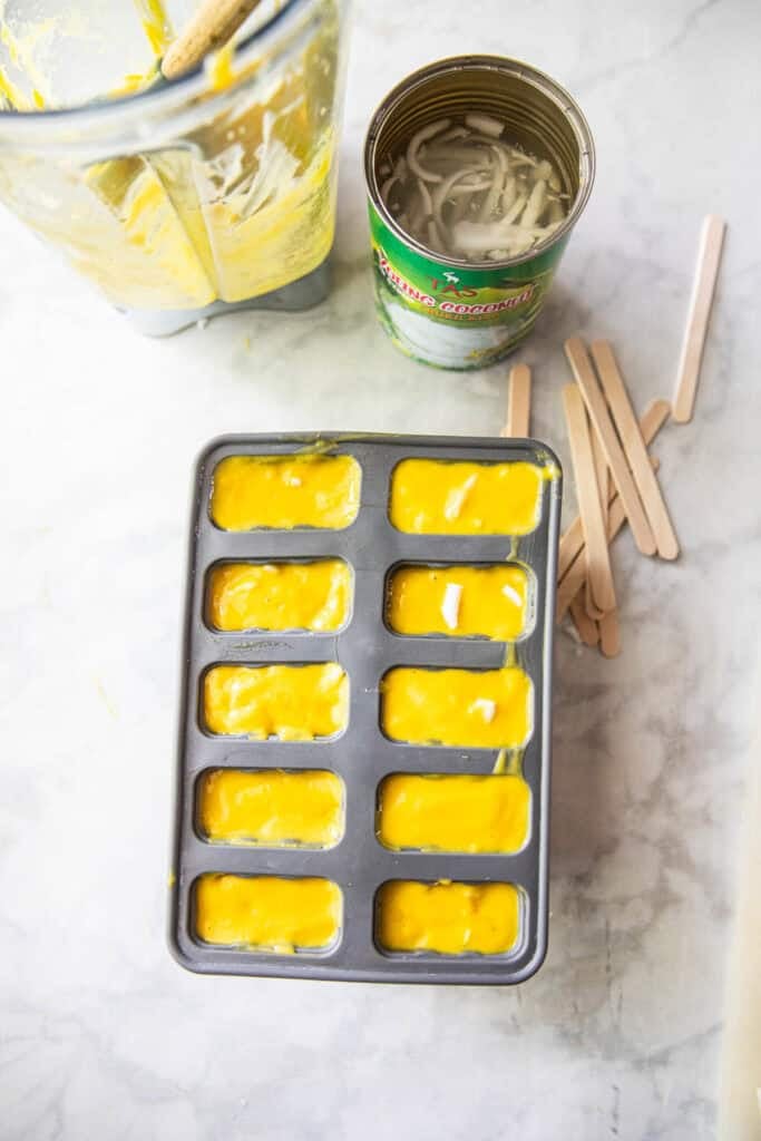 Pureed mango in popsicle molds on a table. 
