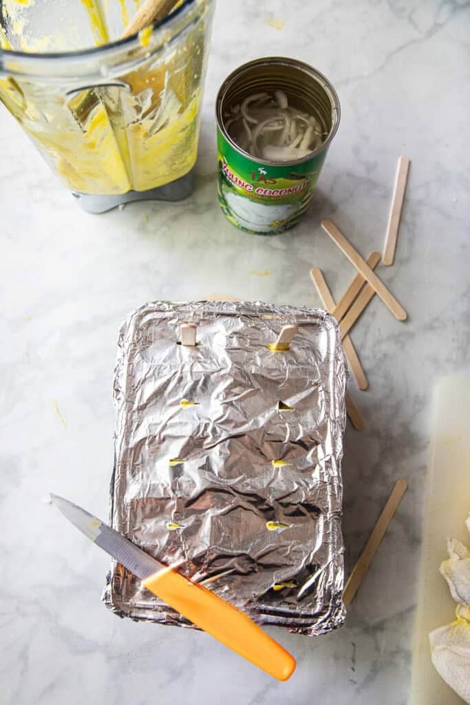 mango pureed in popsicle molds with aluminium foil on top on a table. 