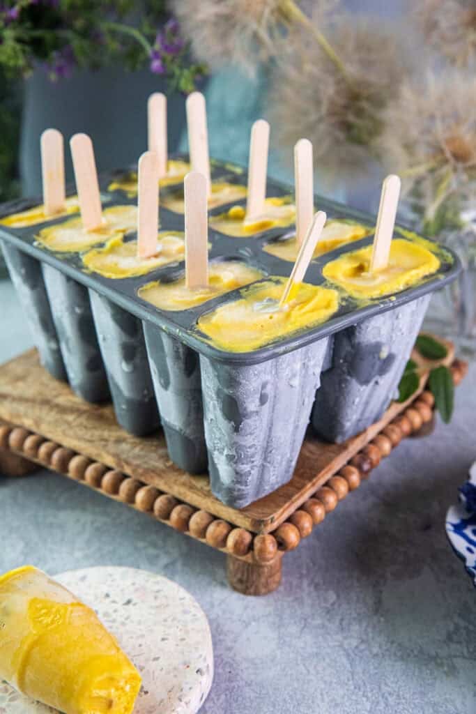 Mango popsicles in molds, sitting on a table. 