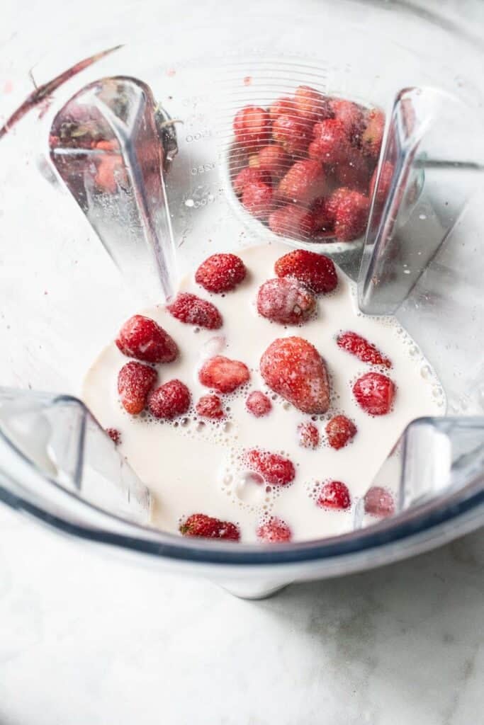 Strawberries and milk in a food processor on the table.