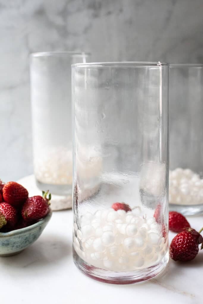 3 glasses of white boba pearls on a table with strawberries on the side. 