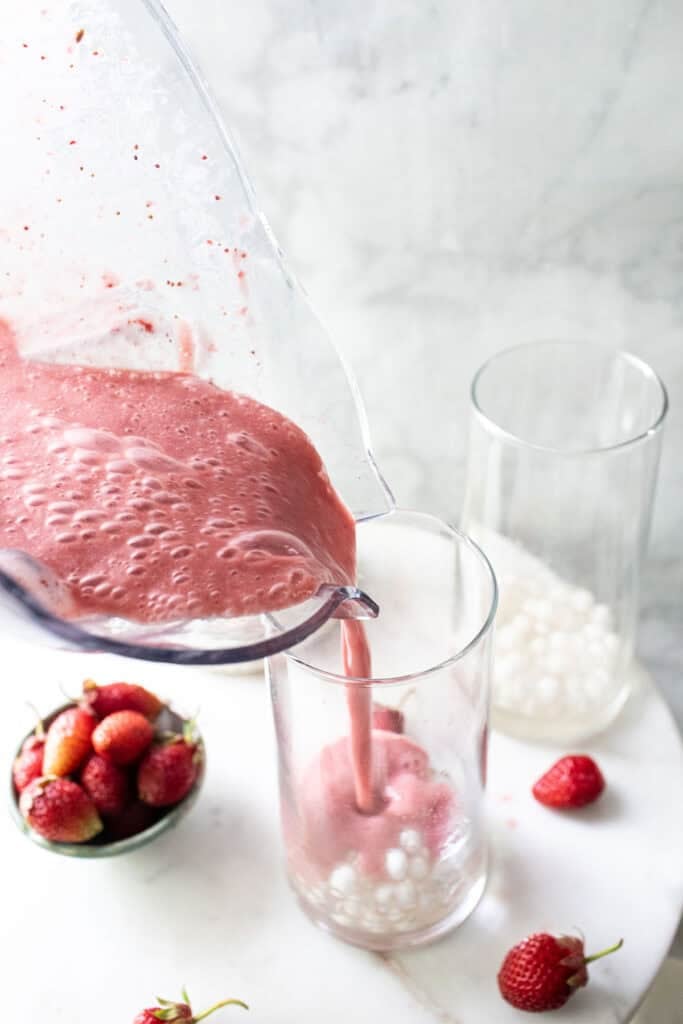 Puree strawberry pouring into a glass with white boba pearls for making Oat milk strawberry boba.