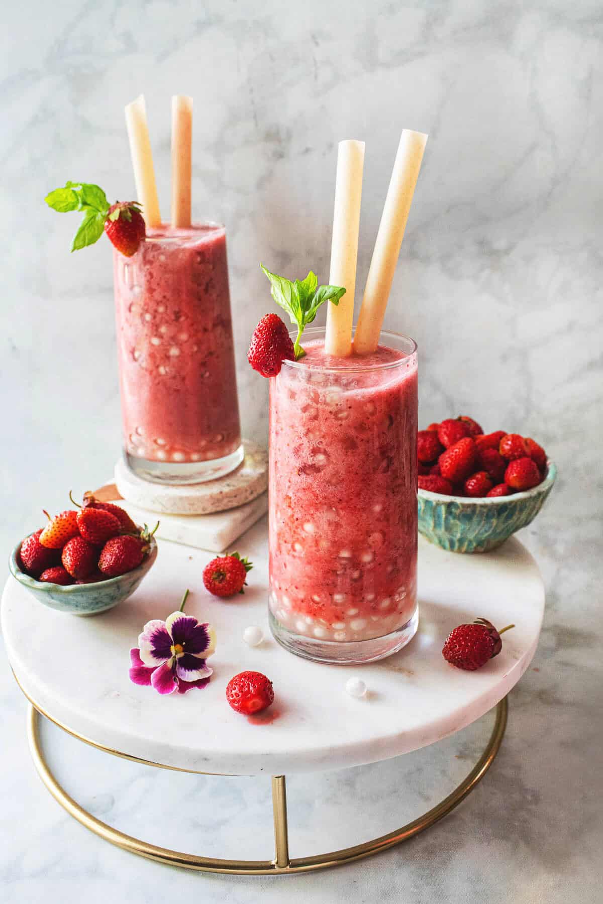 Two glasses of Strawberry boba are on the table with strawberries in bowls. 