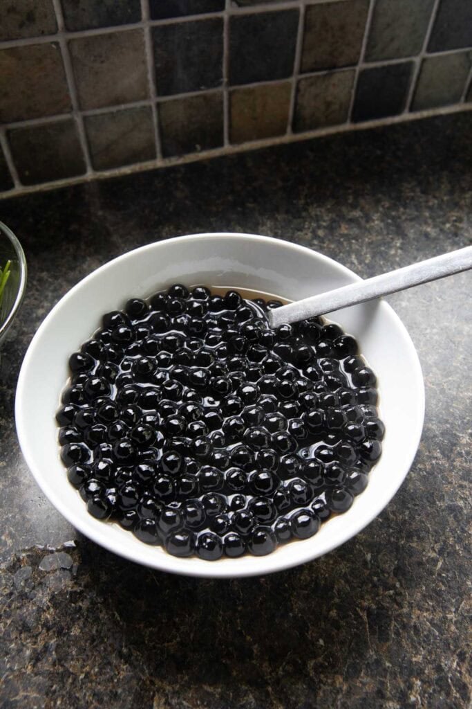 Black boba pearls in a bowl with a spoon in it. 