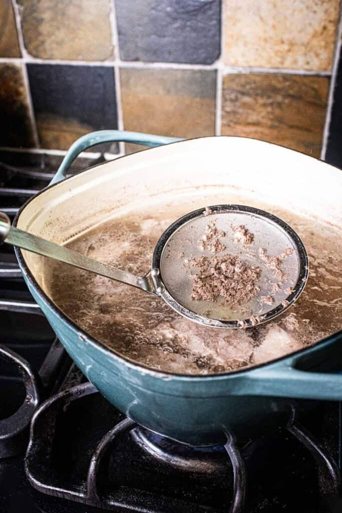 Strainer lifting soup scums from a pot on the stove. 