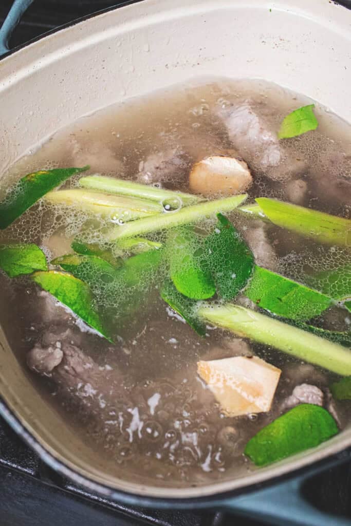 Pork ribs in broth and thai herbs in a pot on the stove.