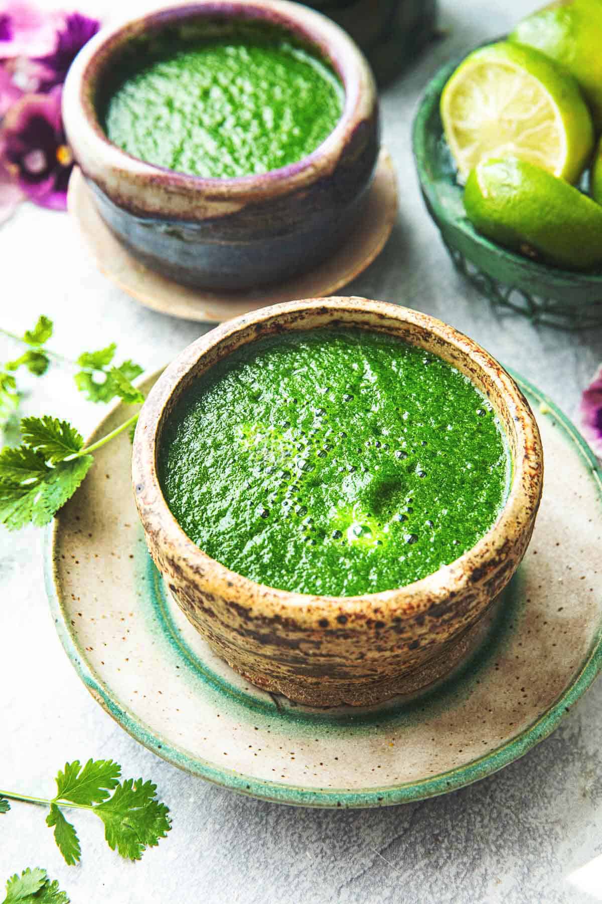 Thai cilantro dressing in a small brown bowl on top of a platter with cilantro leaves on the sides. 
