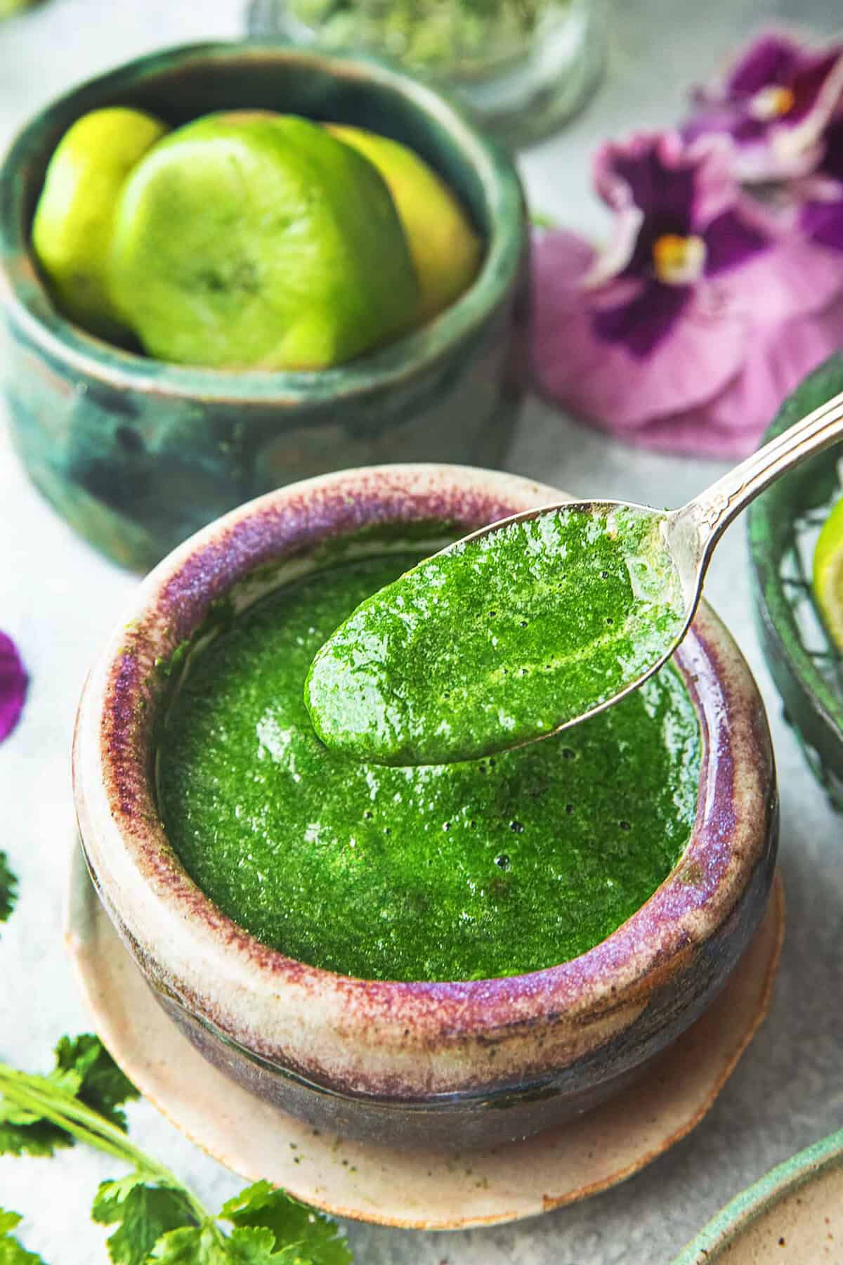 A spoon lifting Thai cilantro dressing from a small bowl on top of a platter with cilantro leaves on the sides. 
