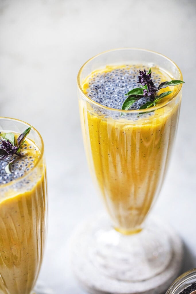 Two glasses of mango smoothie with basil seeds and basil on top as garnish. 