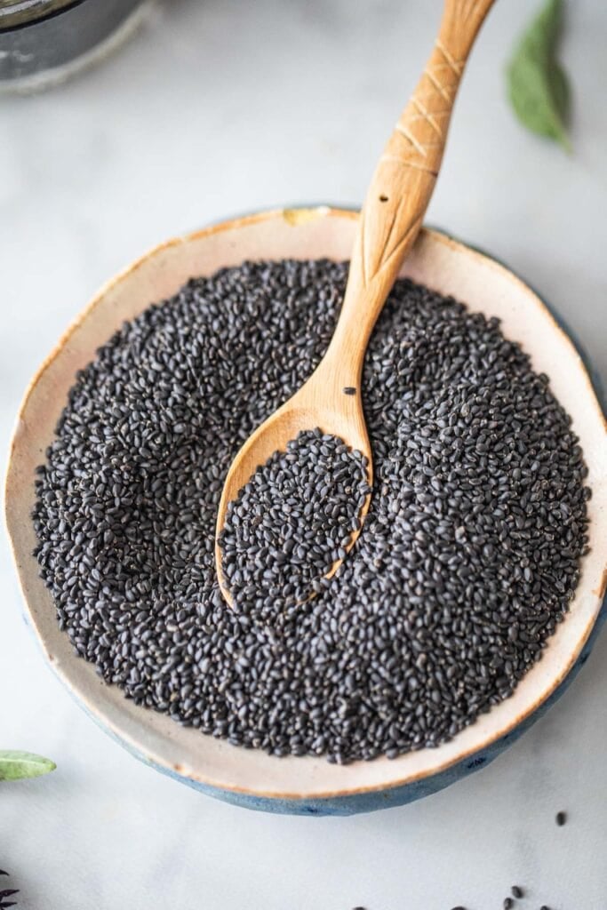 Thai basil seeds on a plate with a wooden spoon in the middle. 